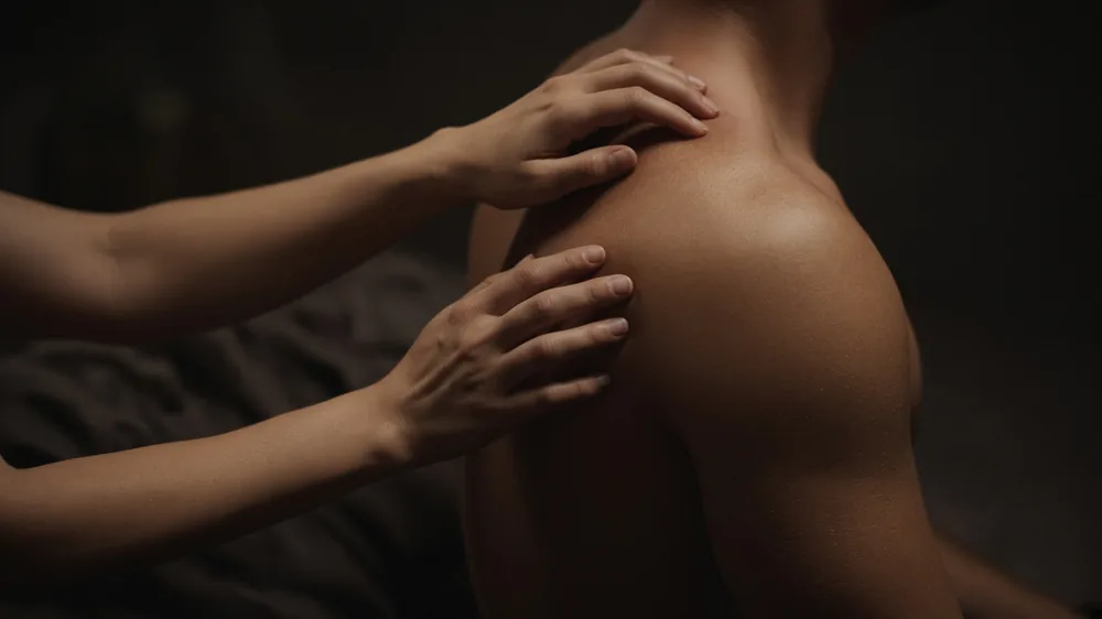 A woman's hands on a man's bare shoulder
