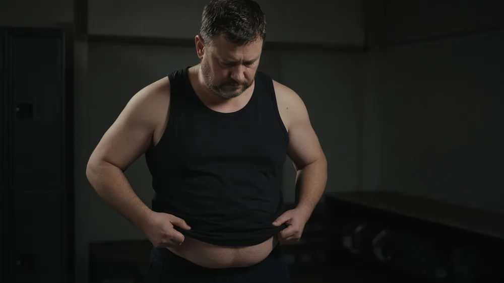 Man pinching the soft belly under his tank top