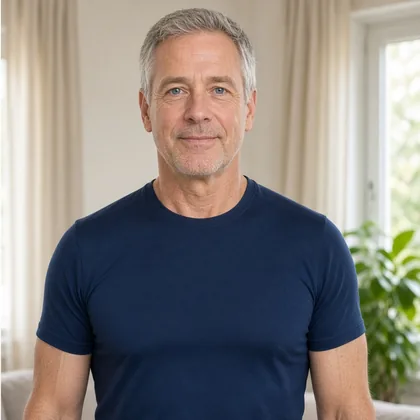 A grey-haired man in a navy T-shirt at home